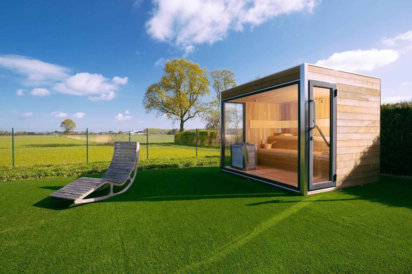 Modern outdoor sauna on artificial turf lawn with lounge chair, showcasing premium synthetic grass for luxury landscaping applications