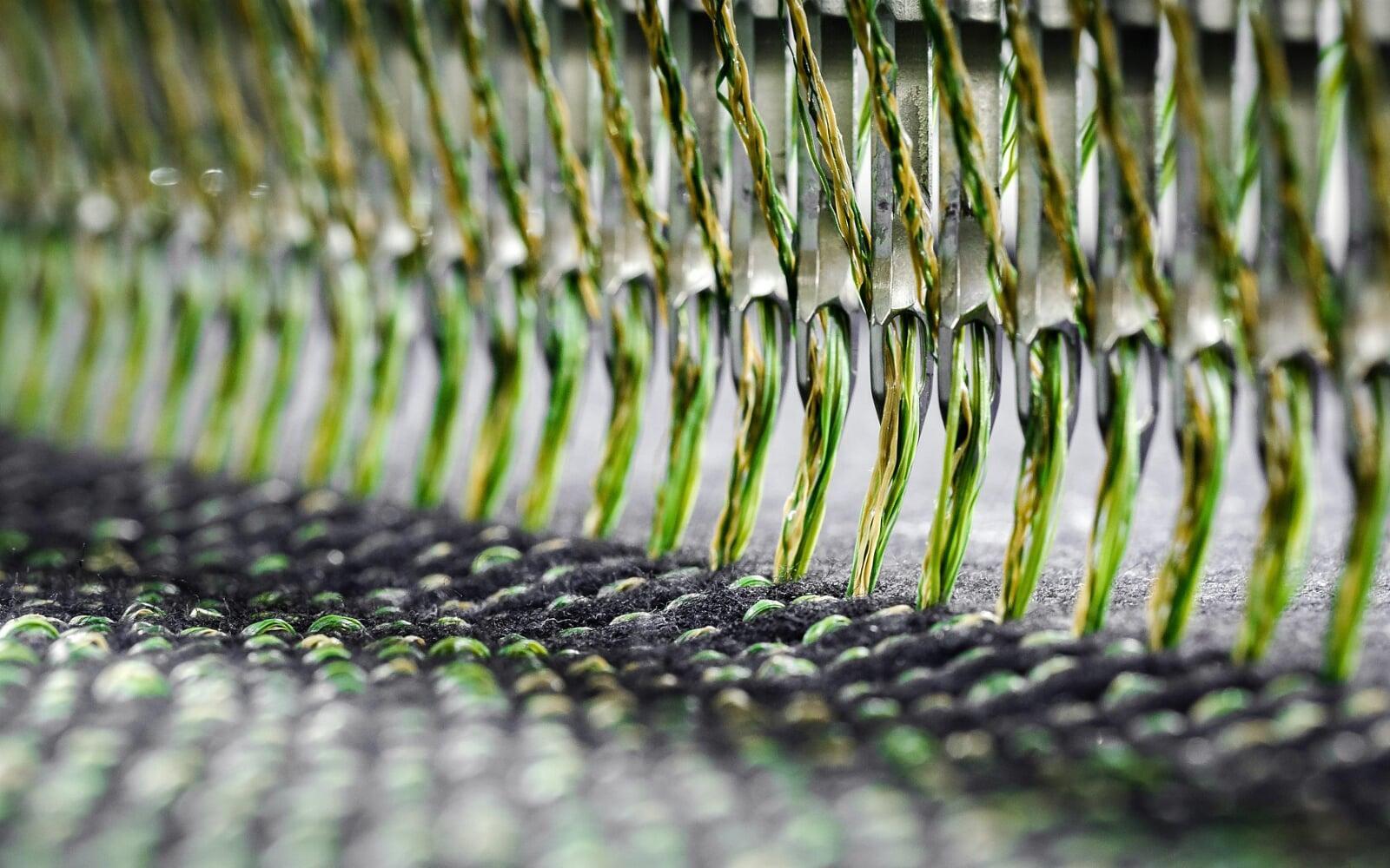 Close-up of tufting needles stitching green yarn into backing, forming high-density artificial turf fibers for durable sports and landscaping surfaces