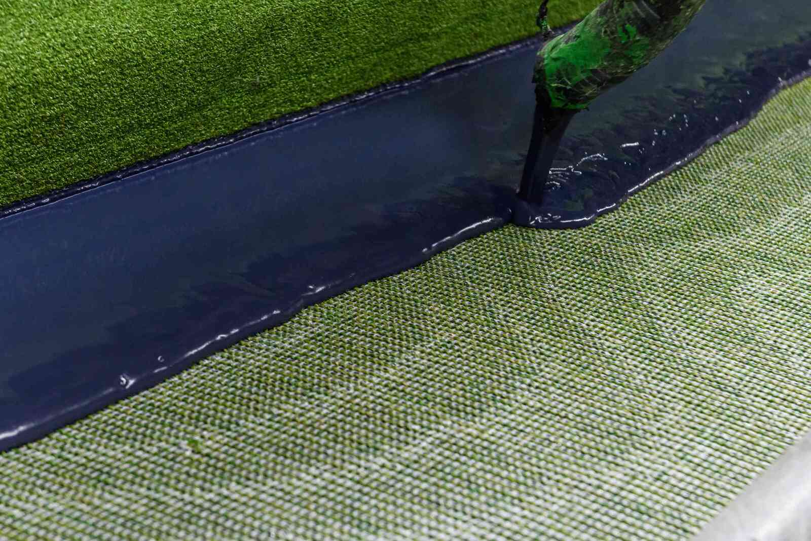 Liquid backing application on artificial turf base layer showing durability engineering for premium synthetic grass performance Liquid backing application on artificial turf base layer showing durability engineering for premium synthetic grass performance