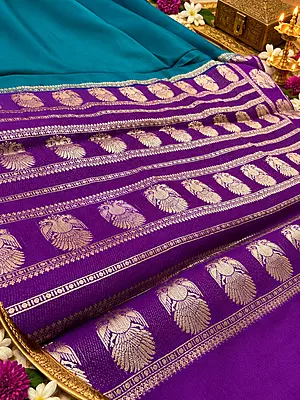 ? ROYAL PURPLE SILK SAREE A stunning royal purple silk saree featuring intricate gold zari weaving, elegant peacock motifs, and a beautifully detailed geometric floral pattern.