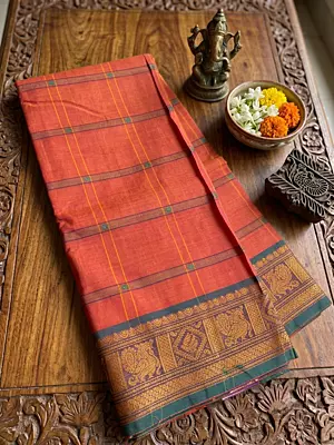 This elegant handloom saree features a vibrant rusty-orange body adorned with traditional grid lines and delicate floral motifs throughout