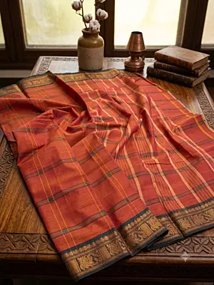 This elegant handloom saree features a vibrant rusty-orange body adorned with traditional grid lines and delicate floral motifs throughout