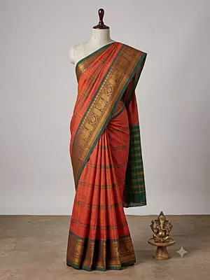 This elegant handloom saree features a vibrant rusty-orange body adorned with traditional grid lines and delicate floral motifs throughout