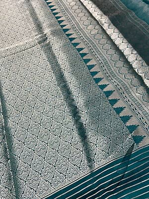 A magnificent dark bottle green silk saree featuring a heavily brocaded body filled with intricate, traditional gold zari weaving pattern