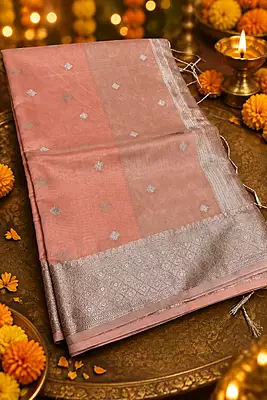 A delicate and elegant peach pink silk saree featuring a subtle tissue-like sheen and beautifully woven silver zari diamond buttas throughout the body.