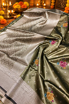 A sophisticated charcoal grey silk saree with a beautiful metallic sheen, featuring delicate silver polka buttas and subtle multicolour floral motifs.