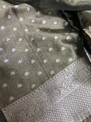 A sophisticated charcoal grey silk saree with a beautiful metallic sheen, featuring delicate silver polka buttas and subtle multicolour floral motifs.