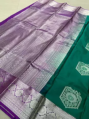 A rich emerald green silk saree featuring elegant silver zari floral motifs beautifully placed across the body.