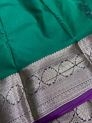 A rich emerald green silk saree featuring elegant silver zari floral motifs beautifully placed across the body.