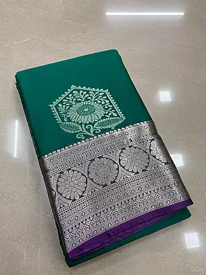 A rich emerald green silk saree featuring elegant silver zari floral motifs beautifully placed across the body.