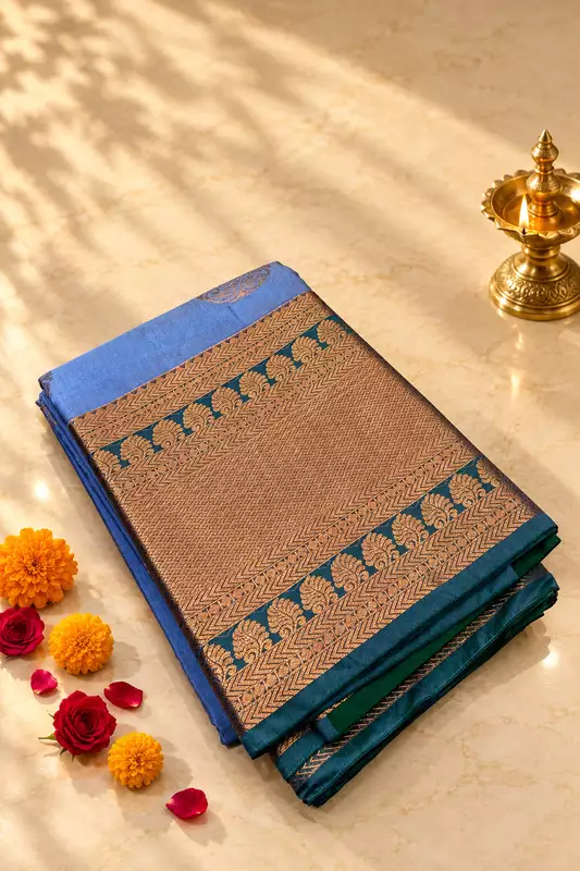 A graceful powder blue silk saree featuring elegant antique-gold paisley motifs scattered across the body.