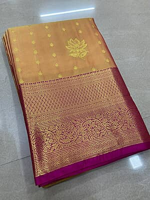 A luxurious peach-gold silk saree with a beautiful lustrous finish, adorned with delicate gold zari buttas and elegant floral motifs