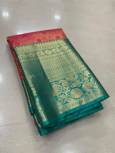 A rich red and teal silk saree featuring an intricate all-over gold zari floral pattern on the body.