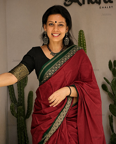 Maroon cotton saree featuring a plain body and detailed green floral border