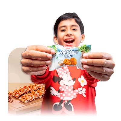 Child holding SIRIMIRI Coconut Laddu highlighting Great Indian Snacks collection Child holding SIRIMIRI Coconut Laddu highlighting Great Indian Snacks collection
