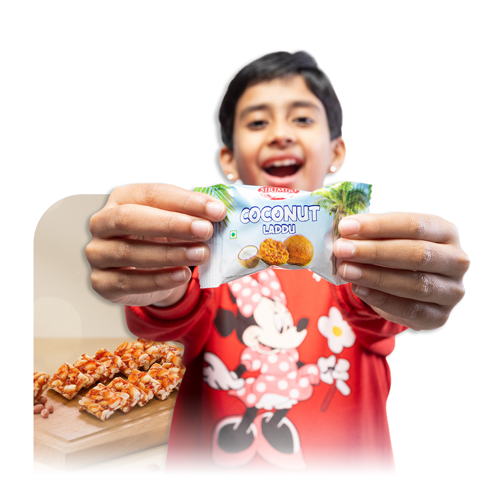Child holding SIRIMIRI Coconut Laddu highlighting Great Indian Snacks collection Child holding SIRIMIRI Coconut Laddu highlighting Great Indian Snacks collection